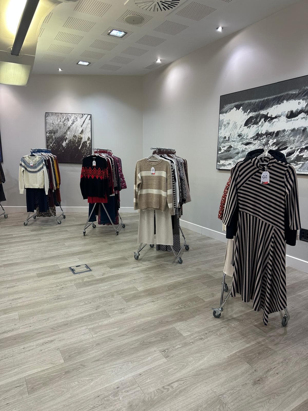 Rincón del showroom con cuadros en blanco y negro y burros de ropa con prendas de punto