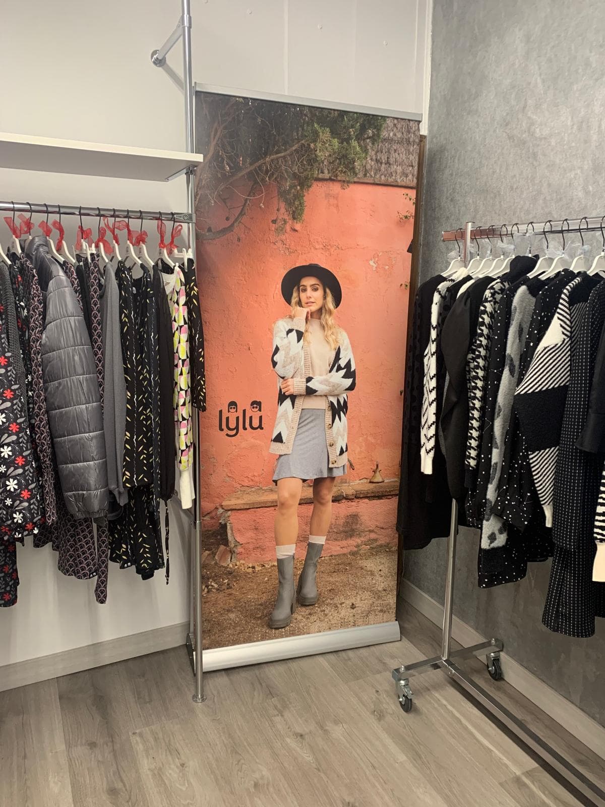 Expositor con la imagen de marca de Lylu entre dos percheros de abrigos y chaquetas
