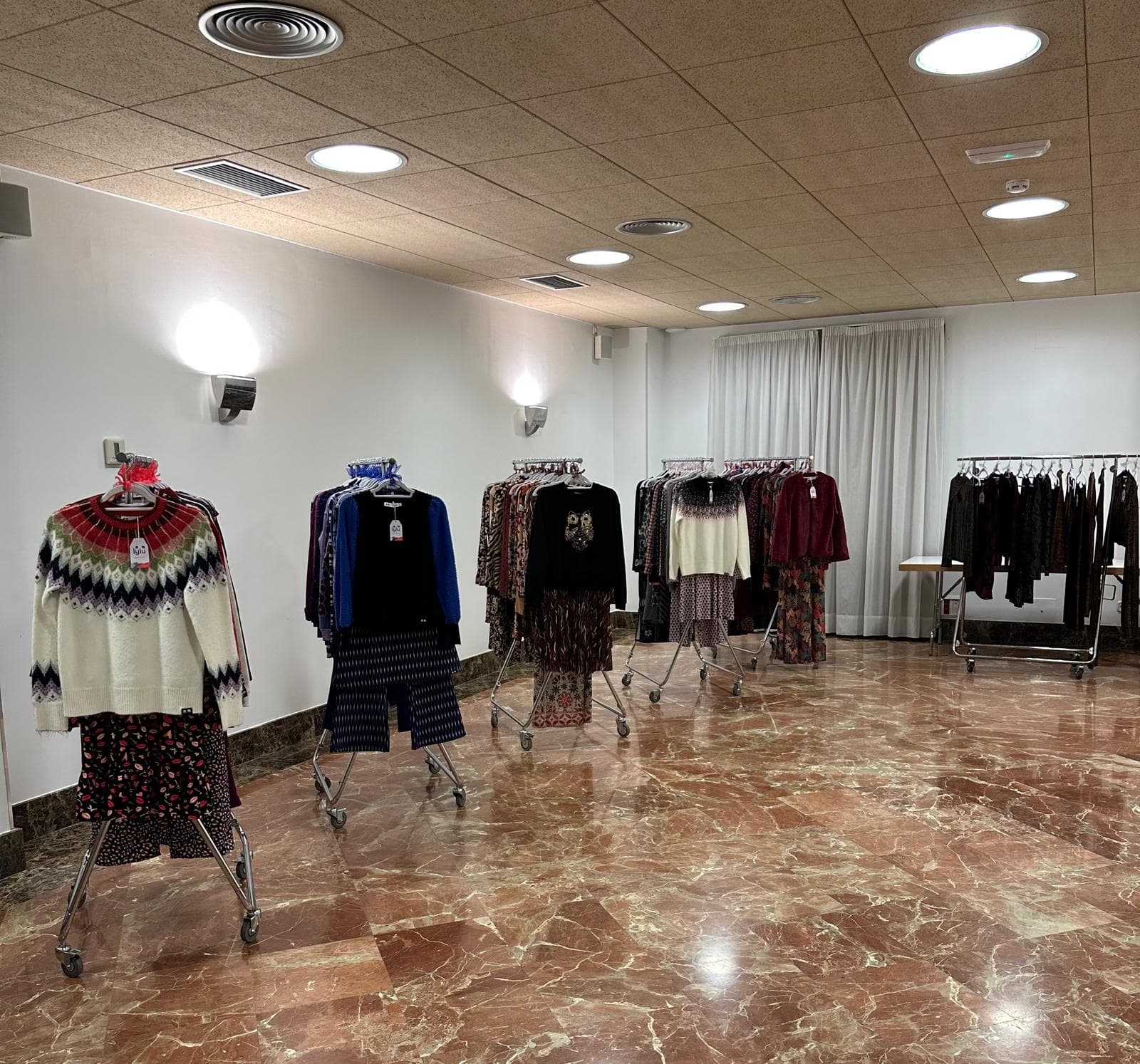 Vista general de la sala con maniquíes de punto y percheros de temporada sobre suelo de mármol